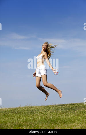 Happy woman in bikini blanc et shorts les sauts dans un champ vert d'été Banque D'Images
