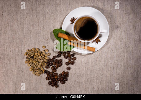 Vue de dessus sur un assortiment de différents types de java beans et les herbes à côté de la vapeur chaude tasse pleine de café et soucoupe sur nappe gris. Banque D'Images