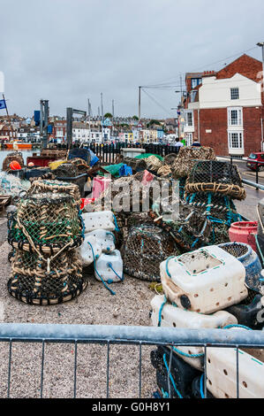 Des casiers à homard et des engins de pêche soigneusement empilés sur le côté port prêt à charger dans un bateau de pêche dans le port très animé de Weymouth Banque D'Images