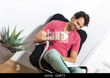 Homme assis sur un fauteuil avec un verre et livre Banque D'Images