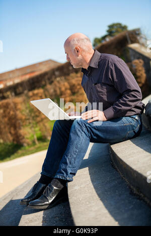 Homme assis sur un banc à l'aide d'un ordinateur portable Banque D'Images