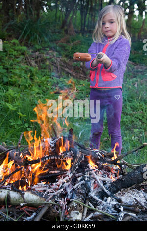 Fille de préparer et de manger des saucisses cuites sur feu de camp Banque D'Images