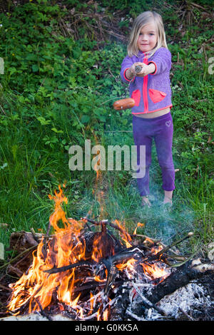 Fille de préparer et de manger des saucisses cuites sur feu de camp Banque D'Images