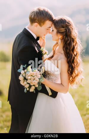 Senior jeune mariée et le marié avec bouquet rubbing noses outdoors Banque D'Images