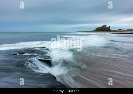 Le bruit de la mer comme il l'ebbs retour après une vague s'écraser sur la plage de Bamburgh et château de Bamburgh en arrière-plan. Banque D'Images