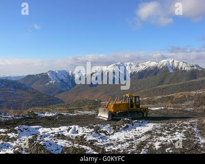 Tracteur à chenilles avec grederom sur fond de montagnes enneigées Banque D'Images