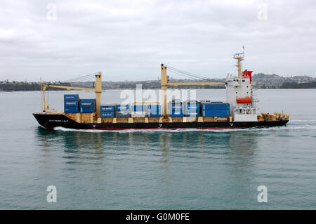 Porte-conteneurs le sud de Lily têtes hors de l'Auckland Harbour avec des conteneurs de transport et des voitures sur le pont. Banque D'Images