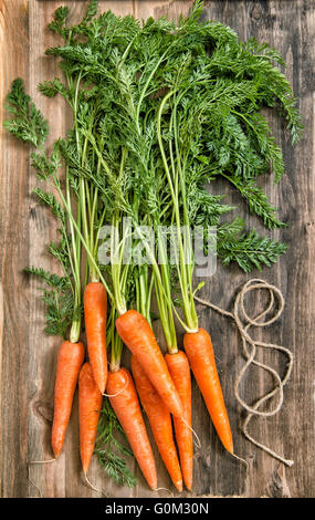 Racines de carottes fraîches avec des feuilles vertes sur fond de bois rustique. Concept d'aliments biologiques Banque D'Images