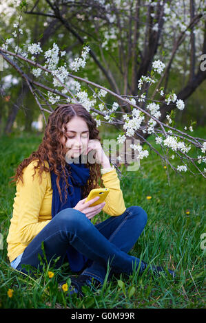 Belle jeune femme assise sur l'herbe avec un smartphone Banque D'Images