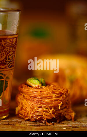 Libre d'un verre décoré avec du thé et une pâtisserie baklava surmontée de pistaches sur une table en bois rustique Banque D'Images