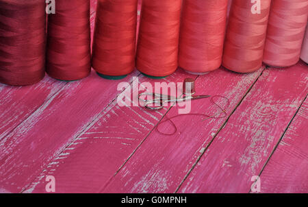 Un certain nombre de bobines de fil dans les tons rouges avec des objets pour la couture sur la table Banque D'Images