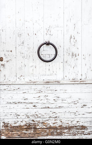 Porte en bois blanc patiné avec un anneau en métal et bouton serrure rouillée texturé avec peinture blanche écaillée et peeling. Banque D'Images