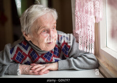 Une vieille femme est assise et regarder par la fenêtre. Banque D'Images
