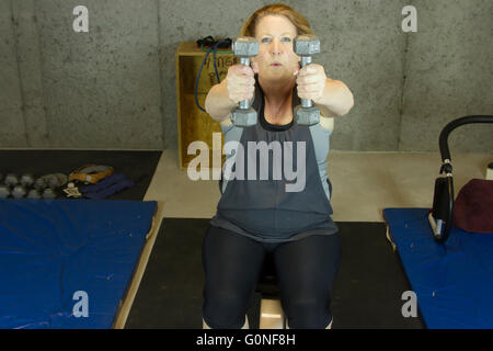 Femme mature en sous-sol salle de sport en utilisant des poids libres pour renforcer la partie supérieure du corps. Banque D'Images