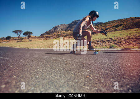 Side portrait of young woman wearing protective gear longboard en plein air sur une route. Banque D'Images