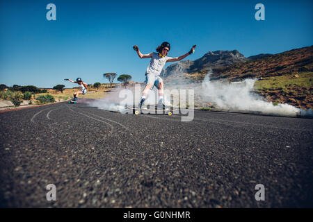 Tourné en plein air de jeunes gens patiner dans la rue. L'homme et la femme la pratique de patinage. Conseil long avec grenade fumigène. Banque D'Images