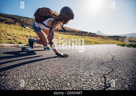 Jeune femme à cheval sur sa planche à roulettes. La patineuse de patinage artistique féminin pratique sur route de campagne. Banque D'Images