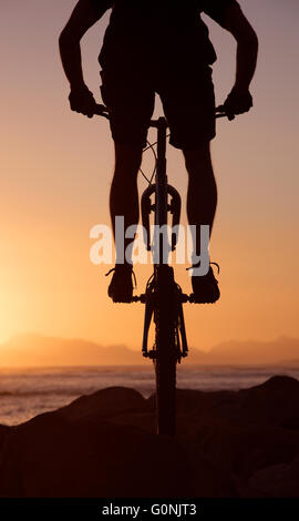 Silhouette d'un mountain bike rider jumping over rocks sur le brin dans le Western Cape Afrique du Sud au coucher du soleil. Banque D'Images