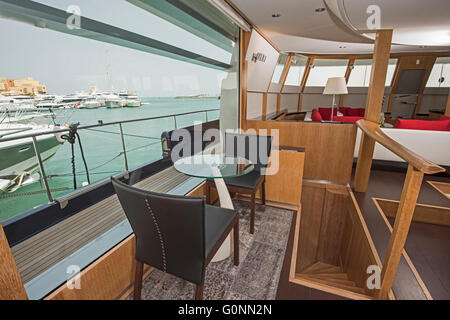 Coin salon dans le salon d'un grand yacht de luxe avec grande fenêtre panoramique montrant vue sur marina de l'océan tropical Banque D'Images