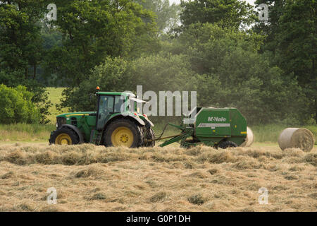 Ensilage - tracteur tirant une ramasseuse-presse travaille dans un champ à grande Ouseburn, North Yorkshire, Angleterre. Banque D'Images