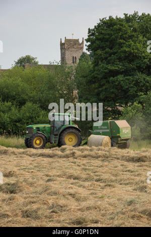 L'ensilage ou le foin de décisions - l'homme est le moteur du tracteur agricole vert tirant une ramasseuse-presse, travaillant dans un domaine - Grande Ouseburn, North Yorkshire, Angleterre, Royaume-Uni. Banque D'Images