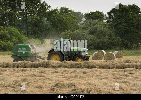 Tracteur agricole travaillant dans un champ, ensilage et tirant une ramasseuse-presse à balles rondes (4 balles au-delà) - Grande Ouseburn, North Yorkshire, GB. Banque D'Images