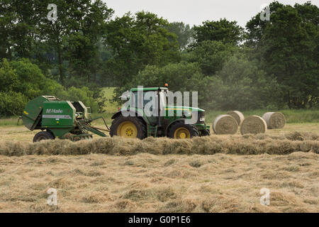 Tracteur agricole vert travaillant dans un champ, l'ensilage ou le foin en balles rondes, tirant des balles cylindriques (4) - au-delà de Grand Ouseburn, North Yorkshire, GB. Banque D'Images