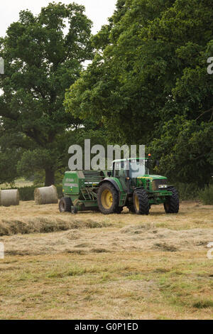 Ensilage, Great Ouseburn, North Yorkshire, Angleterre - tracteur agricole travaillant dans un champ, tirant une ramasseuse-presse à balles rondes au-delà. Banque D'Images