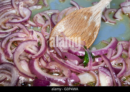Sauteing en remuant les oignons rouges avec cuillère en bois dans la casserole, gros plan Banque D'Images