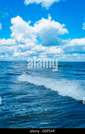Mer du Nord soleil du printemps ciel bleu avec des nuages et une déferlante avec vue lointaine d'un parc éolien offshore Banque D'Images