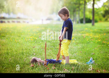 Deux petits garçons, tenant des épées pointées, avec un visage fou à l'autre, la lutte contre l'extérieur, dans le parc Banque D'Images