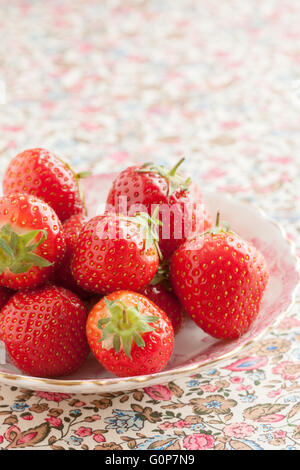 Petit groupe de fraises fraîches sur une petite plaque porcelaine antique. La plaque est sur un joli tissu à motifs floraux. Banque D'Images