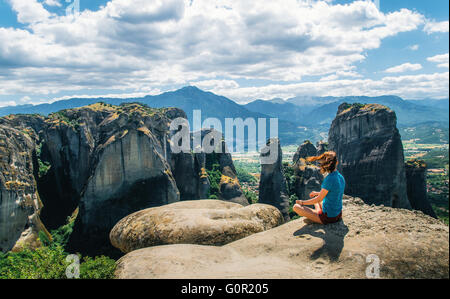 Jeune femme siège au sommet de la montagne et se penche sur les rochers. Traveler appréciant les paysages de montagne des météores, Grèce Banque D'Images