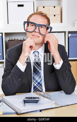 Pensive business man avec surdimensionné lunettes nerd au bureau Banque D'Images