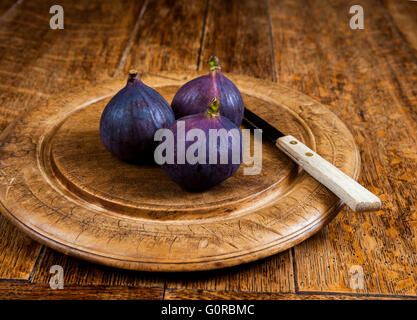 Ensemble de trois figues fraîches sur une planche en bois, qui est sur une table en bois. Banque D'Images