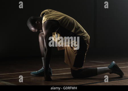 Basket-ball prépare à jouer avec genou sur le plancher et la tête baissé Banque D'Images