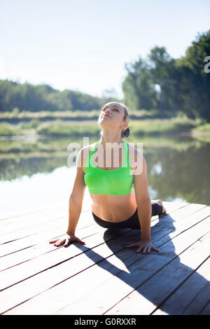 Belle jeune femme blonde fit sportive en vert sportswear working out à l'extérieur, sur le ponton en bois sur le lac Banque D'Images