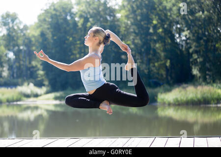 Serene young belle femme flottant dans les airs au cours de la pratique du yoga, de léviter au-dessus du terrain en Eka Pada Rajakapotasana Banque D'Images