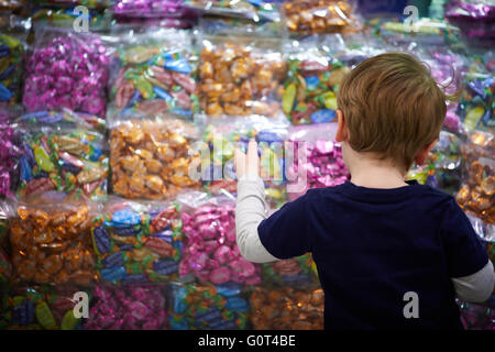 Petit garçon à la recherche de sucreries à travers une vitrine afficher des chocolats sucre qui veulent de l'argent de poche l'achat acheteur vous harceler Banque D'Images