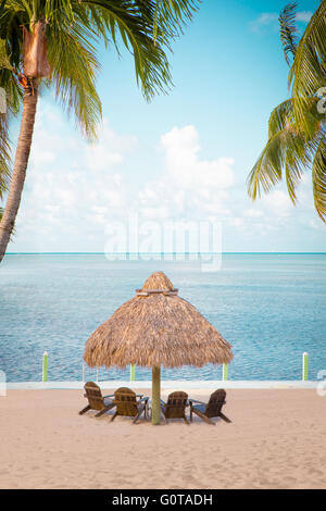 Vacances reposantes à la plage Vue d'herbe hut et des chaises sur le sable face à l'océan avec des palmiers Banque D'Images