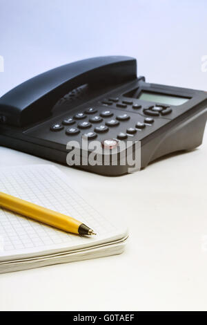 Téléphone IP noir, carnet et un stylo sur fond blanc Banque D'Images