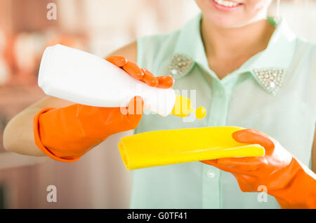 Libre de womans mains porter des gants orange verser les liquides de nettoyage en bac jaune Banque D'Images