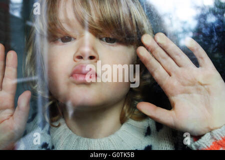 Close-up portrait of boy appuyant sur les lèvres et les mains contre la vitre Banque D'Images