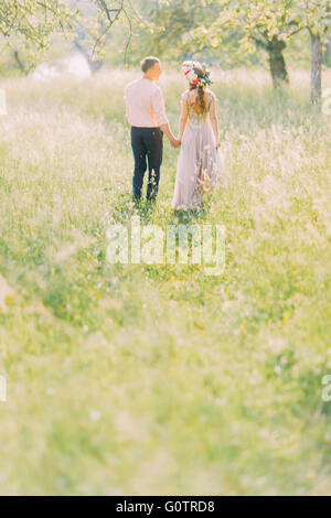 Couple in love walking holding hands, young man and woman wearing wreath sur date, regarder, vue arrière Banque D'Images