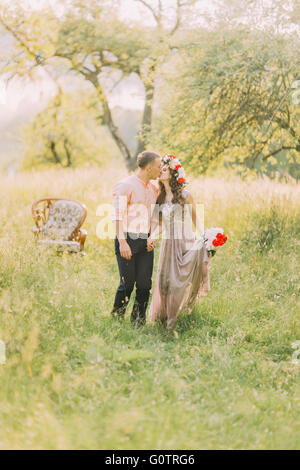 Jeune couple romantique et embrasser dans jardin, chaise en bois sur l'arrière-plan Banque D'Images