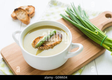 Un bol de soupe aux asperges blanches avec asperges et pain organisée sur une planche à découper avec la ciboulette Banque D'Images