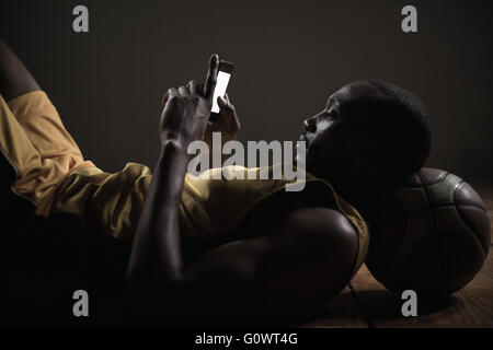 Portrait de joueur de basket-ball de mensonge et de l'aide de son smartphone Banque D'Images