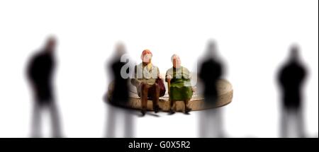 Une figurine miniature couple âgé assis sur un pound coins en face de 4 hommes hors foyer Banque D'Images