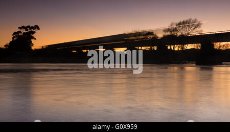 Passage du train sur un pont de la rivière à l'aube. Banque D'Images