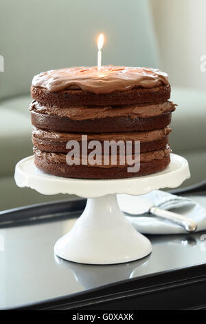 Gâteau d'Anniversaire Chocolat en couches avec bougie allumée on Cake Stand sur table basse Banque D'Images